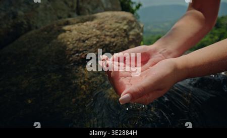 Gros plan des mains humaines ventant doucement l'eau de source de montagne claire sur la pierre naturelle dans le paysage forestier vert Banque D'Images
