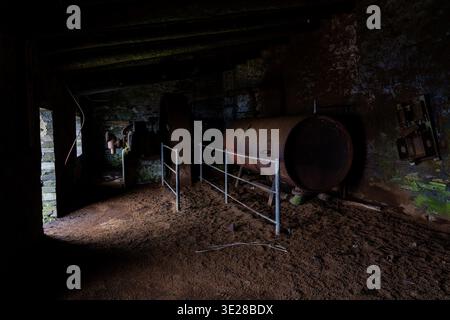 Réservoir en fer altéré et équipement mécanique derrière des garde-corps métalliques à l'intérieur d'un bâtiment en pierre abandonné dans la carrière d'ardoise de Dinorwic Banque D'Images