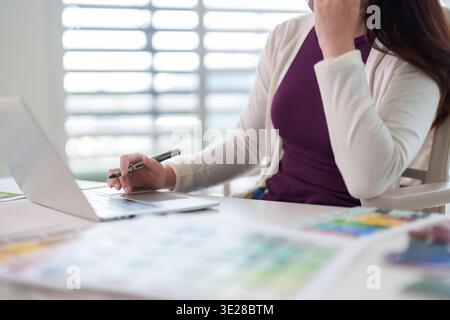 La femme concentrée s'engage dans des tâches numériques. Elle effectue un travail de conception créative sur un ordinateur portable dans un espace de travail contemporain. Idéal pour les professionnels à distance. Banque D'Images
