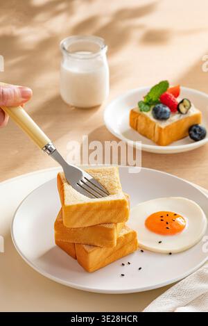 Pile de tranches de pain doré avec une fourchette et un côté ensoleillé vers le haut oeuf frit sur une assiette blanche Banque D'Images