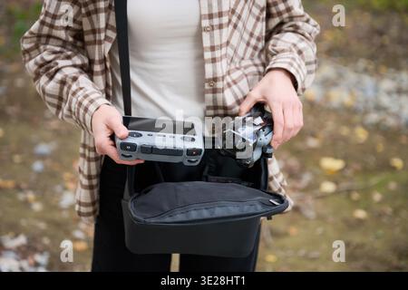 La femme tient le drone et le contrôleur pris dans le sac. Gros plan des mains préparant quadcopter à l'extérieur, organisant l'équipement avant le vol, concept de passe-temps, de préparation et de technologie Banque D'Images