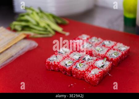 Rouleaux Tobiko rouge vif sur la planche à découper rouge à côté de l'avocat et du couteau, texture Roe brillant et soigné Banque D'Images