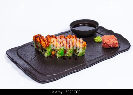 Rouleau garni d'avocat sur plateau noir avec tranches vert vif, garniture ardente, croûte de sésame, wasabi soja Banque D'Images