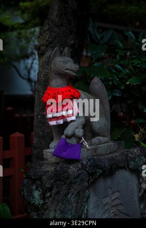 Statue de renard en pierre avec bavoir rouge et sac violet au jardin du sanctuaire japonais, gardien spirituel Banque D'Images