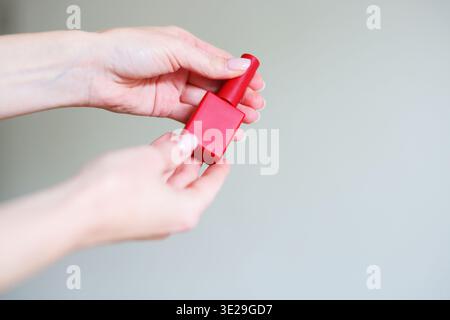 Femme présentant la bouteille de vernis à ongles rouge dans les mains. Concept de manucure, de soin des ongles et de produit de beauté cosmétique Banque D'Images
