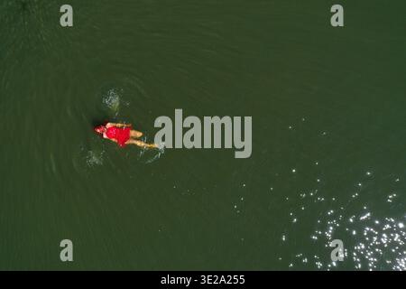 Vue aérienne d'une magnifique femme en robe rouge flottant sur l'eau calme par drone Banque D'Images