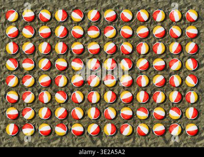 Rendu 3D de boules de plage gonflables disposées dans une grille répétitive régulière sur une surface de plage de sable texturée. Banque D'Images