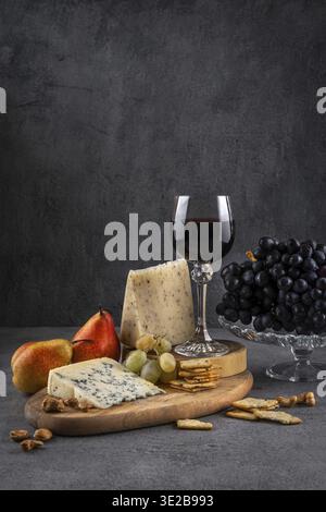 Verre de vin rouge avec fromage bleu et raisins sur fond sombre. Vin rouge avec fromage et fruits. Espace pour le texte Banque D'Images