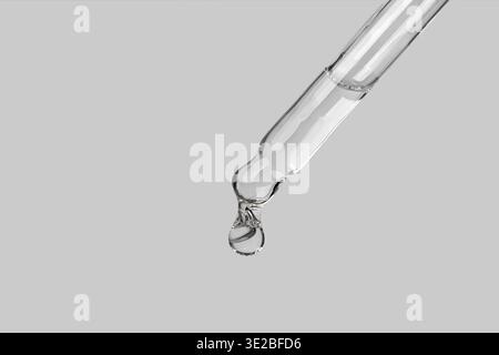 Pipette gros plan avec sérum ou huile essentielle avec une goutte tombante. Une goutte de sérum hydratant tombe de la pipette Banque D'Images