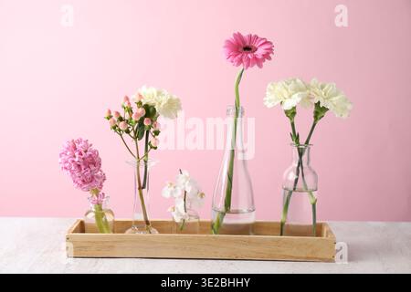 Belles fleurs dans des vases sur une table blanche sur fond rose Banque D'Images