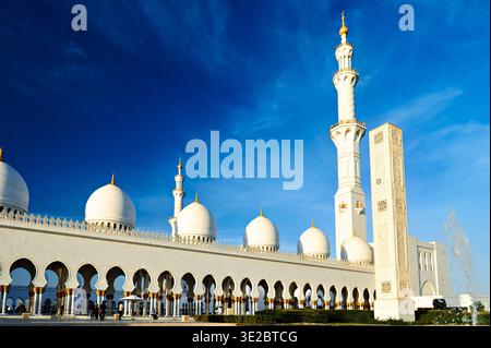 Les gens explorent la Grande Mosquée Sheikh Zayed à Abu Dhabi sous un ciel bleu clair. La mosquée met en valeur sa belle architecture. Banque D'Images
