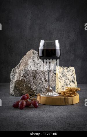 Verre de vin rouge avec fromage bleu et raisins sur fond sombre. Vin rouge avec fromage et fruits. Espace pour le texte Banque D'Images