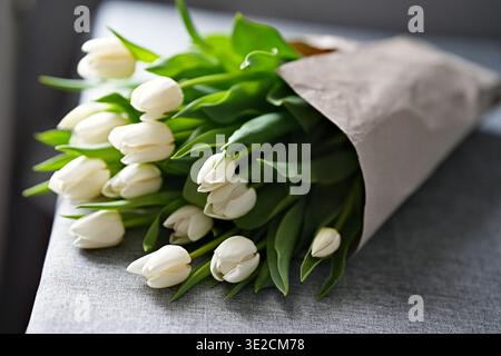 Un bouquet de tulipes blanches enveloppées dans du papier d'emballage simple repose sur la table. Photo horizontale Banque D'Images