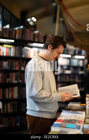 Homme intelligent concentré examinant le manuel dans la librairie à la mode, inspectant à travers le contenu du roman populaire Banque D'Images