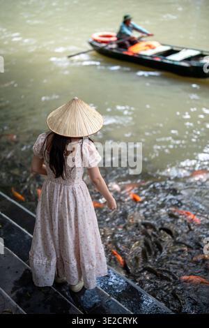 Femme nourrissant des carpes koï colorées dans l'étang, activité de loisirs relaxante positive pour les touristes au Vietnam Banque D'Images