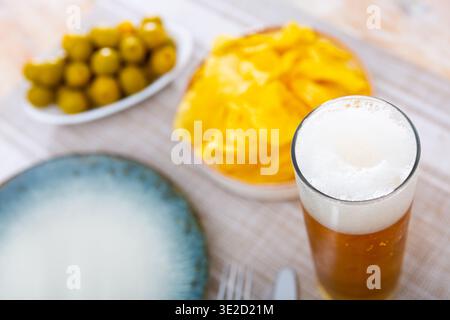 Verre de bière fraîche mousseuse avec en-cas - chips et olives marinées. Banque D'Images