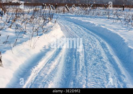 Une piste de motoneige fraîchement tracée serpente à travers un paysage hivernal lumineux sous la lumière du soleil, projetant des ombres bleues sur la poudreuse intacte Banque D'Images