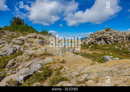 Sentier de pierre serpentant à travers un terrain rocheux vers un petit lac alpin avec des sommets montagneux lointains. Banque D'Images