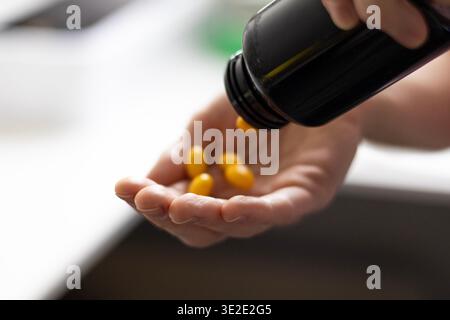 Gros plan de capsules de vitamine jaune versées d'une bouteille dans une main. Routine quotidienne de supplément, soins de santé, concept de soutien immunitaire Banque D'Images