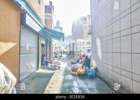 Les vendeurs se rassemblent dans une ruelle ensoleillée au marché. La chaleur de la lumière du soleil et des ombres de l'hiver soulignent une routine matinale paisible. Banque D'Images