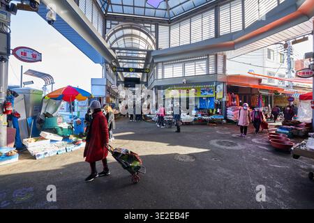 Les vendeurs se rassemblent dans une ruelle ensoleillée au marché. La chaleur de la lumière du soleil et des ombres de l'hiver soulignent une routine matinale paisible. Banque D'Images