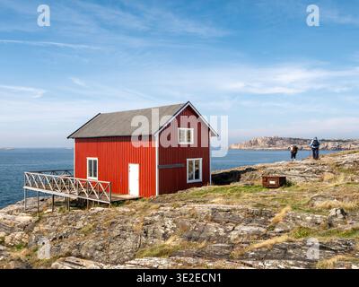 Deux personnes marchant à proximité maison en bois rouge sur la côte rocheuse à Åstol, Bohuslän, côte ouest de la Suède Banque D'Images