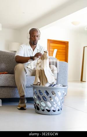Homme adulte africain assis sur le canapé gris pliant chemise beige du panier à linge dans le salon Banque D'Images