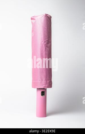 Élégant parapluie pliant compact en rose pastel doux, soigneusement enroulé et fixé avec une sangle, avec une pointe en métal brillant et un logo subtil. Banque D'Images