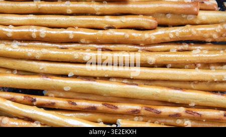 Texture de fond gros plan de bâtons de bretzel salés. Collations salées croustillantes alignées horizontalement, montrant des cristaux de sel et une croûte brune dorée Banque D'Images