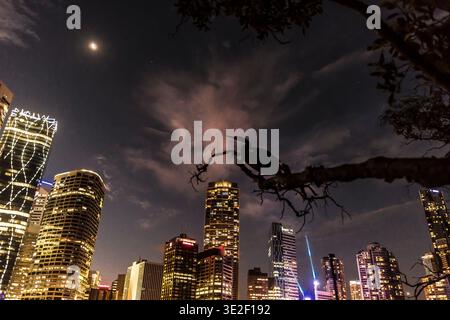 Paysage urbain nocturne avec des bâtiments illuminés et une silhouette perchée plus sombre au premier plan. Banque D'Images
