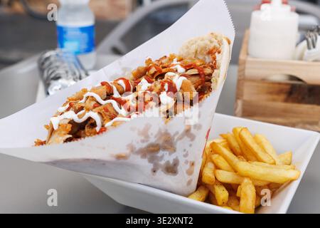 Gros plan d'un kebab de poulet avec sauce blanche et rouge servi avec des frites Banque D'Images