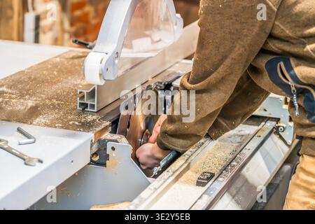 Une menuisière guide une planche de bois à travers une scie à table, assurant une coupe droite et précise dans un atelier de menuiserie bien équipé Banque D'Images