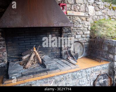 Un espace barbecue extérieur rustique traditionnel avec une grande hotte métallique, intérieur en brique et bois de chauffage empilé prêt pour l'éclairage. La structure en pierre Banque D'Images