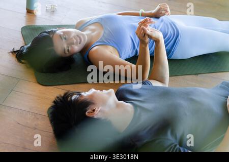 Couple asiatique couché sur des tapis de yoga verts sur plancher en bois tenant les mains près de la bouteille d'eau Banque D'Images
