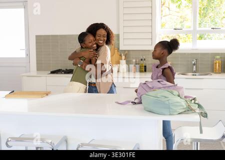 Vidéo verticale : embrasser maman et fille dans une cuisine lumineuse, se préparer à l'école avec des sacs à dos Banque D'Images
