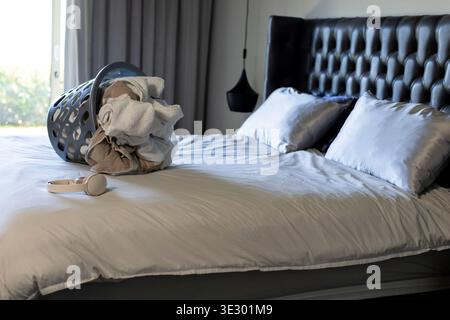 Montrant le lit avec couette gris clair grondant dans la chambre, avec panier à linge renversé des serviettes Banque D'Images