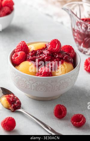 Sorbet à la mangue garni de coulis de framboises et de framboises fraîches. Banque D'Images