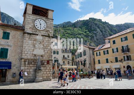 Kotor. Monténégro - 20 mars 2026 : les touristes traversent la place des armes devant la Tour de l'horloge vénitienne historique avec l'ancienne San Giovanni Banque D'Images
