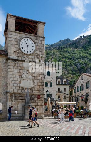 Kotor. Monténégro - 20 mars 2026 : les touristes se rassemblent sur la place des armes sous la Tour de l'horloge vénitienne du 17ème siècle avec l'église de notre garçon Banque D'Images