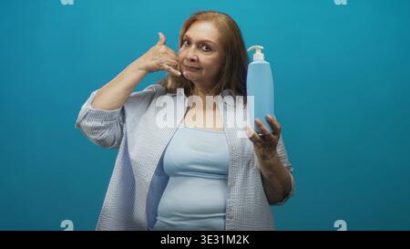 Femme tient une bouteille de savon avec pompe et fait un geste de la main de téléphone dans un studio ; promotion publicitaire d'hygiène ludique. Banque D'Images