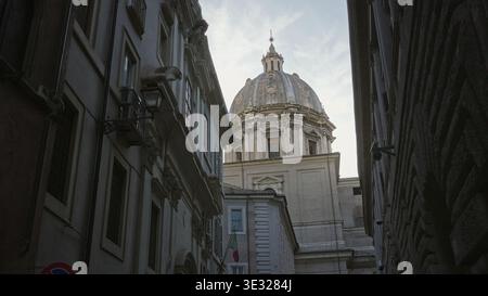 Dôme d'église en pierre au-dessus de la rue pavée étroite avec lanterne et drapeau italien accroché à la façade ; calme historique. Banque D'Images