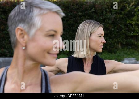 Amies féminines s'étirant sur la pelouse herbeuse dans la cour arrière portant des débardeurs près de la haie taillée et du mur Banque D'Images