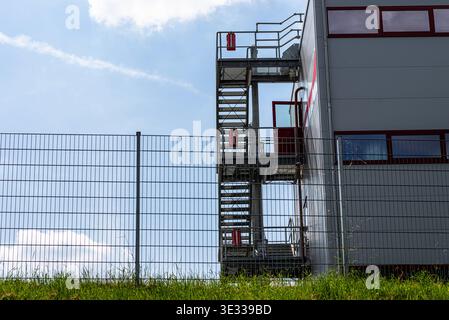 Bâtiment industriel comportant un escalier extérieur en métal avec équipement de secours derrière une clôture de protection Banque D'Images
