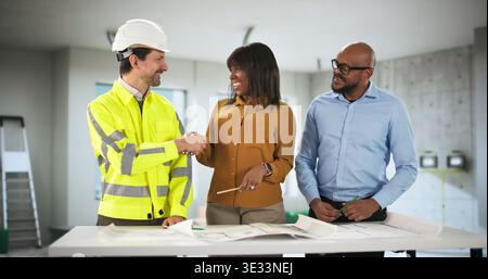 Jeune couple se serrant la main avec l'entrepreneur discutant des plans de rénovation de l'appartement. Le conseiller d'entreprise et l'ingénieur sont d'accord Banque D'Images