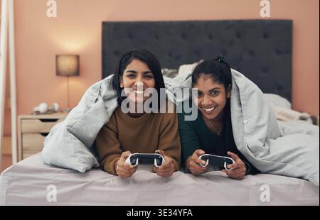 Jeu vidéo, portrait ou frères et sœurs dans la maison avec contrôleur, connexion ou compétition ludique en multijoueur. Femmes heureuses, familiales ou indiennes au lit avec Banque D'Images