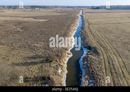 Vue aérienne de la rivière narew partiellement gelée, serpentant à travers des champs secs avec des taches de neige près de Gramotne, voïvodie de podlaskie Banque D'Images