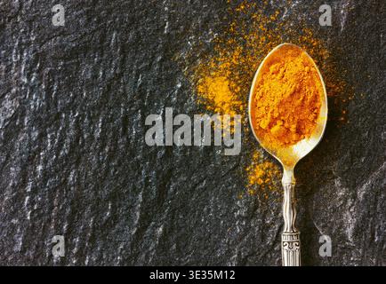 curcuma moulu en cuillère vintage argentée sur la surface de pierre noire Banque D'Images