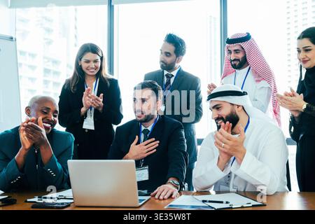 Les membres de l'équipe multiethnique de l'entreprise dans le bureau de dubaï applaudissent et sourient, célébrant une réussite collaborative ou un accord commercial réussi, fost Banque D'Images