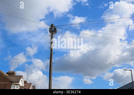 Poteau télégraphique en bois avec plusieurs fils électriques aériens s'étendant vers l'extérieur contre un ciel bleu avec des nuages dans un cadre de rue résidentiel. Banque D'Images