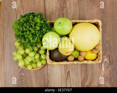 Assortiment de fruits comprenant des raisins, des pommes et des herbes dans un panier sur bois. Assortiment d'aliments biologiques sur table en bois, vue de dessus Banque D'Images